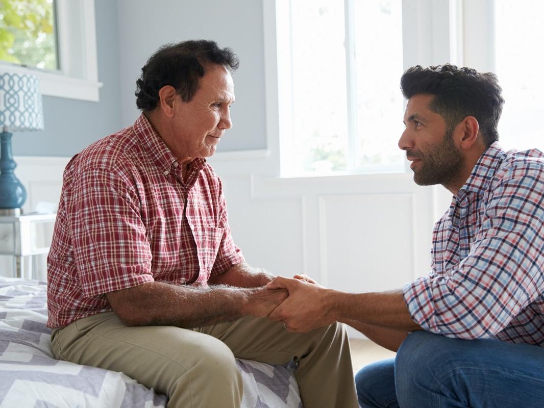 Older father and adult son sitting down talking.